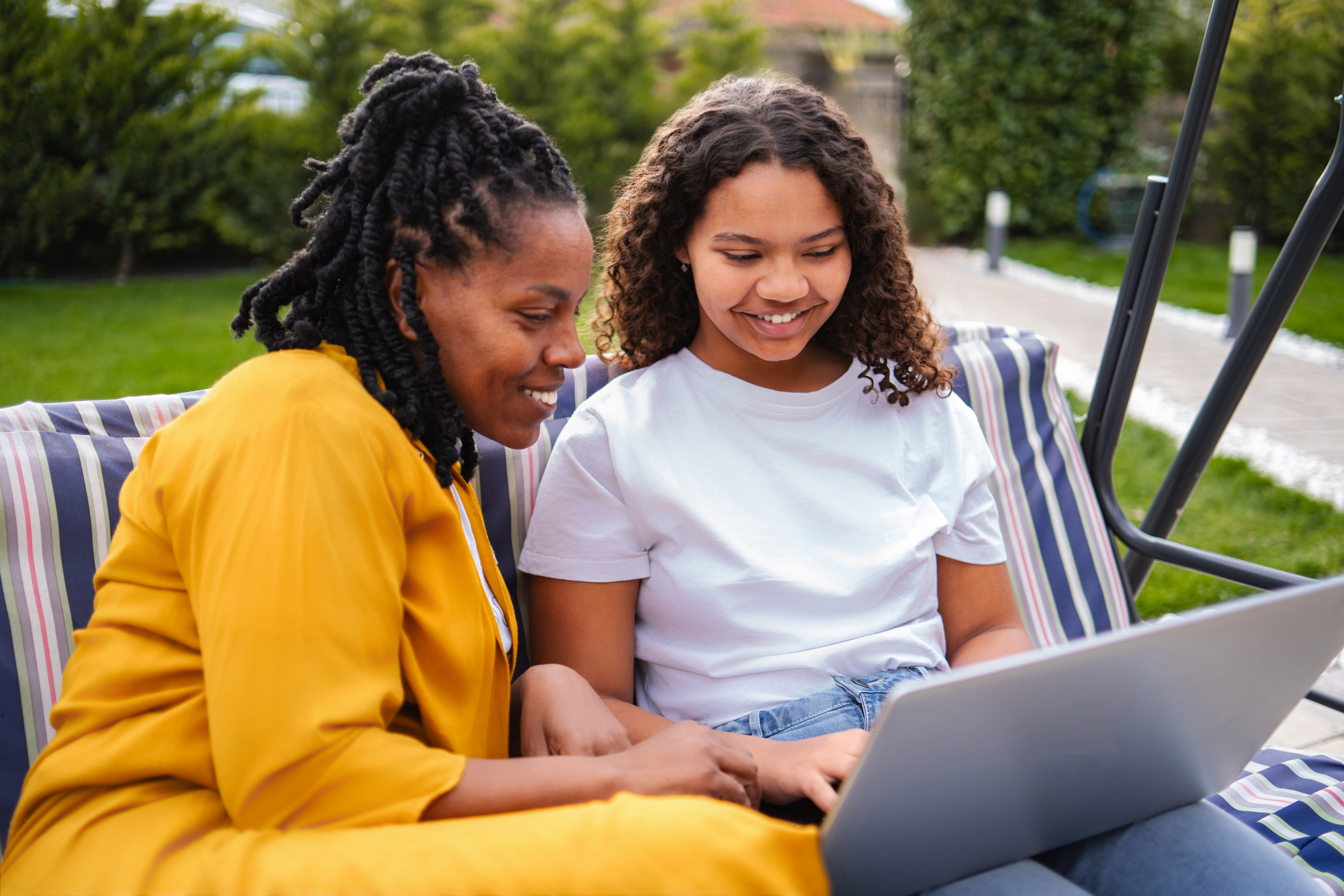 Mother and daughter smiling, spending time together, and using a laptop outdoors